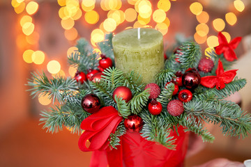 Closeup Small arrangement of fresh spruce with a candle in a ceramic pot. Christmas mood. Bokeh of Garland lights on background.