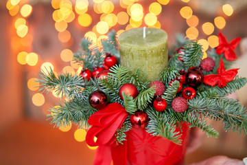 Small arrangement of fresh spruce with a candle in a ceramic pot. Christmas mood. Bokeh of Garland lights on background.