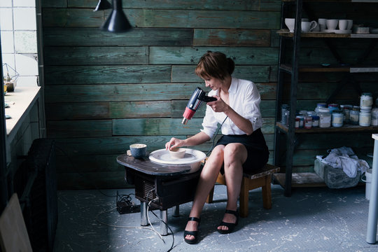 Portrait of Female potter wearing white shirt, business suit working with clay in workshop