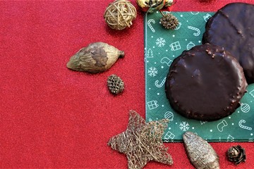 Two selfmade traditional Elisenlebkuchen with chocolate on a green christmas napkin with golden xmas decoration Elements on a red glitter background.. A german specialty.