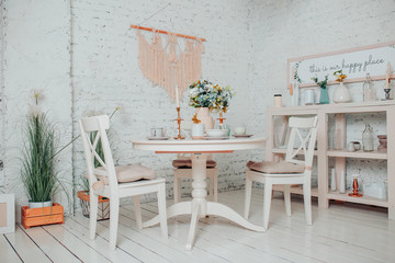 White dining room interior design. White round table with flowers, candles and cups.