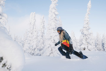 Female snowboarder wearing long dreadlocks and ratsa hoody walking between snow cowered pine trees...