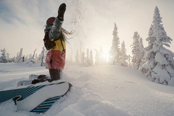 Snowboarder female in rasta color hoodie throwing snow and enjoying fresh powder on  sunset winter...