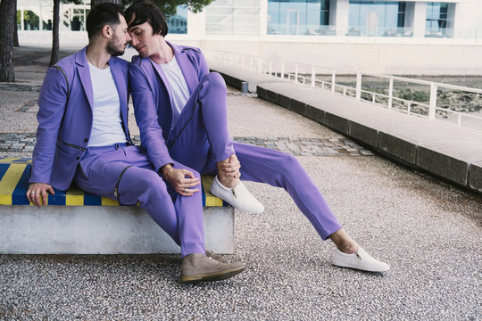 Romantic gay couple wearing purple color suits seating outdoor on seafront together, Happy Wedding walking day