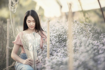 Beautiful young woman traveler looking flowers field sitting on a blurred flowers garden background. Travel holiday relaxation concept. .