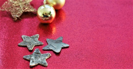 Three wooden stars on a red glitter background with a golden christmas tree ball in the back. Nice xmas decoration concept.