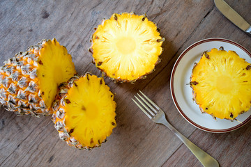 Ripe pineapple slice is served with plate, knife and fork on the wooden table.