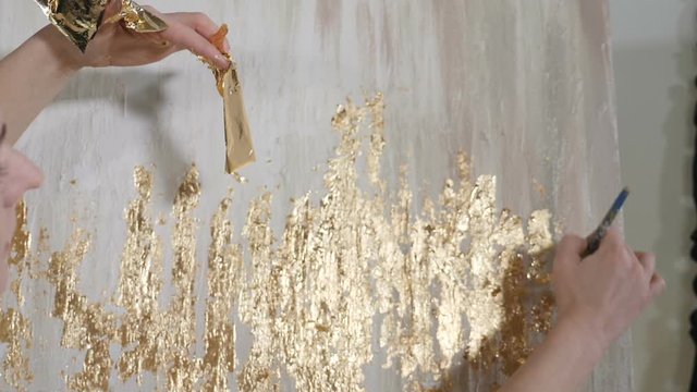 Attractive female artist applying gold leaf to her artwork. Artist decorates picture with tiny sheet of gold. art school, creativity and people concept. Slow motion. Close up. hd