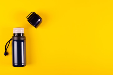 Dark thermos composition on yellow background. Flat lay