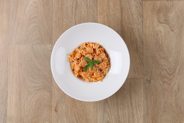 Fusilli with Shrimp pasta with basil leaves and Parmesan cheese in a white plate on a wooden background
