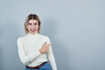 Attractive young unshaven woman in white sweater showing on workspace isolated on gray wall...