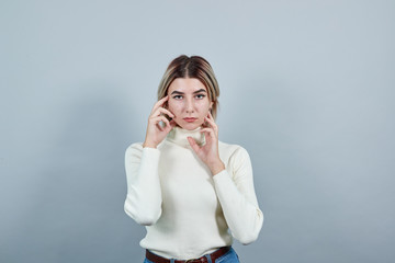 Young beautiful caucasian woman keeping hand on face, model gesture wearing white sweater on isolated white background