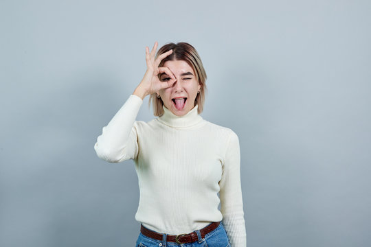 Young beautiful caucasian woman showing ok sign gesture near eyes wearing white shirt on isolated gray background