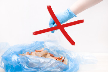 a hand in a rubbery disposable glove puts a plastic cup in a blue bag with organic waste, sorting...