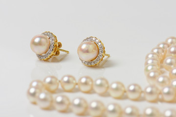 Pair of natural pearl earrings on white with pearl necklace in the background.