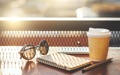 Coffee cup, sunglasses, mobile phone and notebook on desk. people working outdoors with retro style...