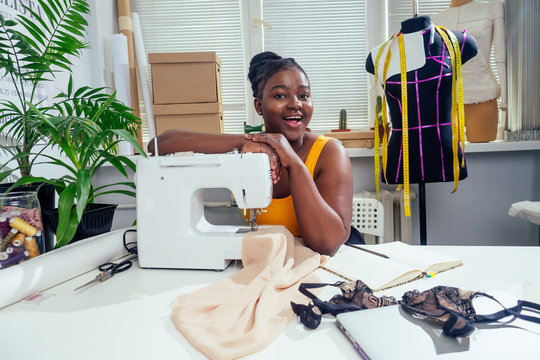 Young african american dressmaker woman sews clothes on sewing machine at tailor office it tropical summer style