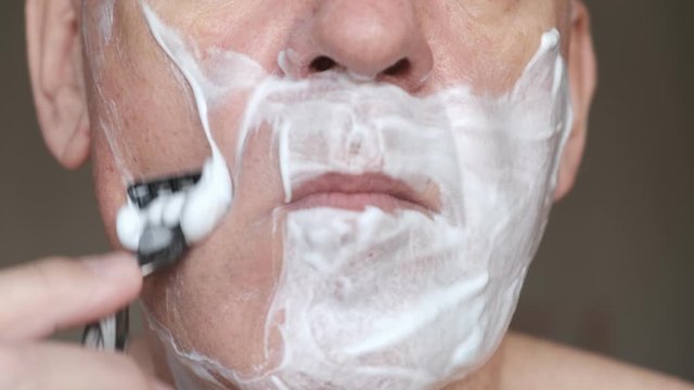 man shaves his beard with shaving foam and a razor