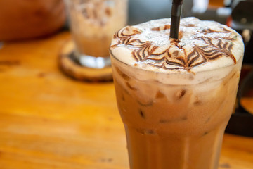 Coffee iced late with milk in plastic glass on wooden table at coffee shop or vintage restaurant with copy space.