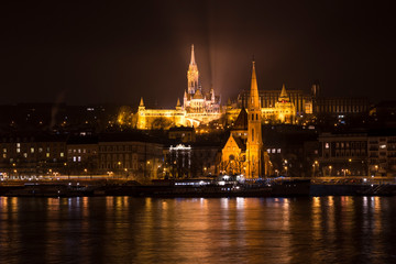 Fototapeta na wymiar Night view through Danube on Buda castle and Matyas cathedral. City Budapest at night. Illuminated Buda castle and Matyas cathedral.