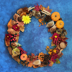 Autumn wreath for harvest festival composition with a variety of natural flora, fauna & food on mottled blue background.   Flat lay, top view.