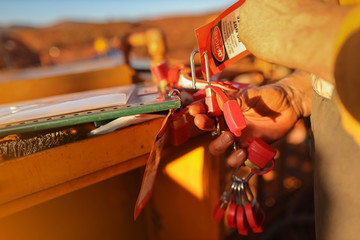 Close up  miner hand placing personal red danger lock which is attached together with danger tag into isolation safety control lock box at the opening field prior to starting each work mine site