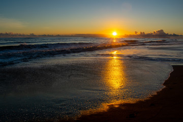 Fototapeta na wymiar A vivid sunset off the beach at Waimea, Kauai, golden sunlight reflecting across the ocean and the wet beach, waves flowing over dark sand.