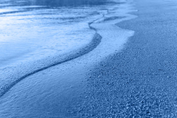 Sea wave and sand seashore in blue colored tone. Sunlight over the sea ocean waves. MIrror reflection on water surface. Macro close up.