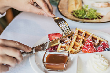 Delicate waffles with fresh strawberries and cream for breakfast. Hands of a girl with cutlery at the table.Black and white photo.