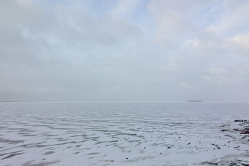 The shore of the Gulf of Finland and frozen water in winter in cloudy weather in classic blue.