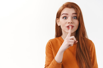 Enthusiastic cute and silly redhead female with long ginger hair asking keep promite, not tell anyone, hiding secret, gossiping, pressed index finger to lips and shush, hush gesture, white background