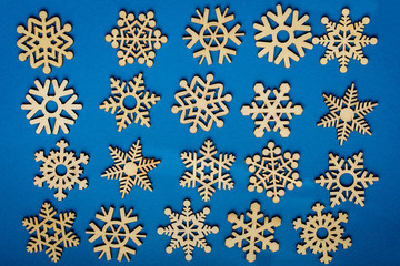 Different delicate light brown wooden snowflakes on vivid classic blue textured cardboard background, displayed as a flower, top view or flat lay with laser cut wooden objects
