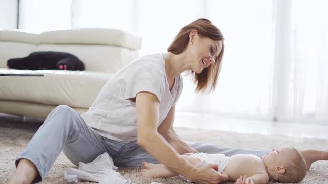 Happy Caucasian mother changing pants on her baby in the living room at home. Shot in 4k resolution
