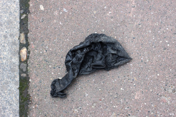 Gloomy deflated black balloon on street sidewalk close up