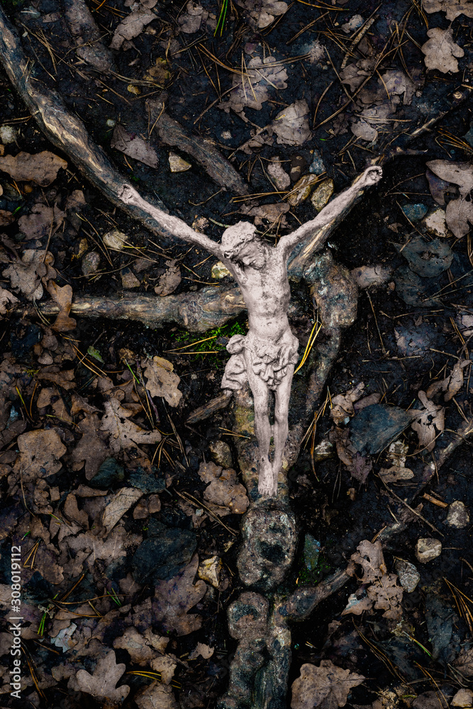 Wall mural Metallic crucifix on tree roots on the ground