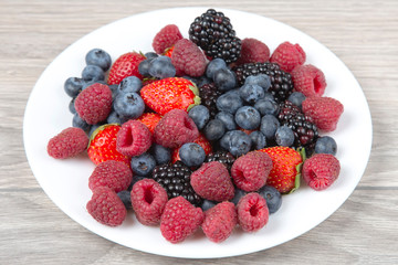 Blackberry, raspberry blueberry and strawberry on a white plate. Vitamins and wholesome foods