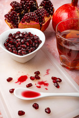 top view, on a rough red background, a heart-shaped bowl with pomegranate seeds, parts of pomegranate and fresh juice in the glass.