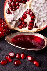 in the foreground a spoon with pomegranate juice and in the background part of the pomegranate with seeds