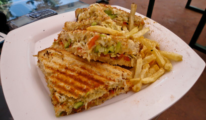 Veg grilled sandwich with french fries, sauce and chilli flakes. Morning breakfast of hot grilled sandwich contains smashed potatoes and vegetables