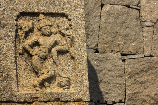 An ancient carving of a four handed Hindu God on a stone wall in the ruins of the Vijayanagar Empire in Hampi, India.