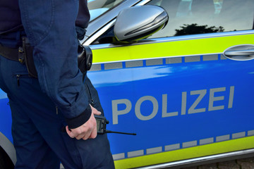 A policeman beside a german police car with a mobile radio in his hand.