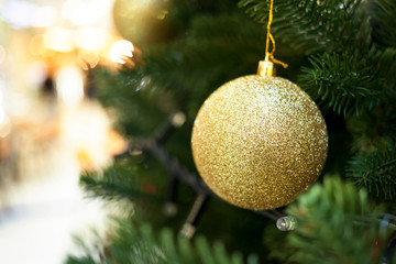 Ball of gold color hangs on a Christmas tree in a shopping center.