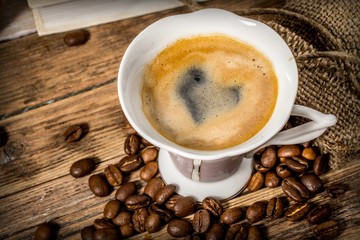 Cup of coffee with a heart painted in foam and beans scattered from a bag on a wooden table