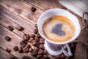 Cup of coffee with a heart painted in foam and grains scattered from a bag on a wooden table