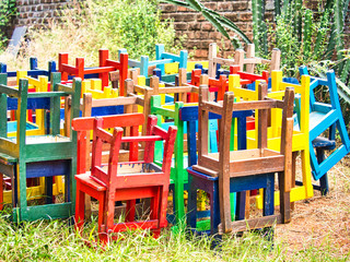 Fototapeta na wymiar Stack of assorted colored wooden chairs in random disarray, full frame furniture background image