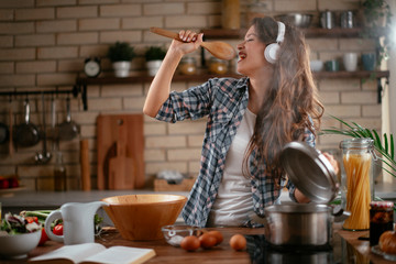Young woman in kitchen. Beautiful woman singing and dancing while cooking. Woman listening music while cooking.