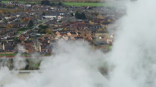 Aerial view of houses through steam at a paper mill, industrial conceptual shot of housing next to industry.