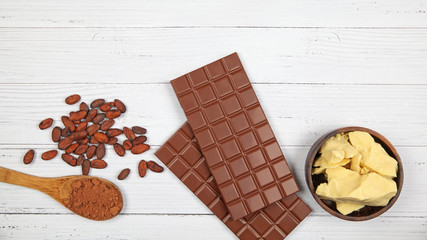 Bars of milk chocolate, cocoa butter, cocoa powder and cocoa beans on light wooden background