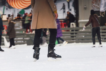 Handsome man in beige coat and black pants skating. Outdoor recreation, winter leisure. Outdoor skating rink in the middle of the city. Winter and seasonal concept. Selective focus, blurred background