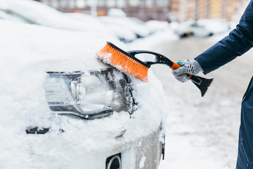 Cropped photo of woman hand in grey mitten brushing the snow from the headlights of a car....